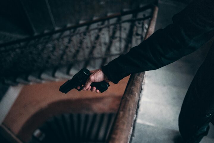 Arm holding a gun on a dimly lit spiral staircase, creating a tense atmosphere.