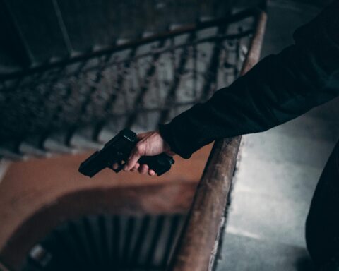 Arm holding a gun on a dimly lit spiral staircase, creating a tense atmosphere.