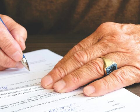 Close-up of a senior adult signing a legal document with a focus on hand and gold ring.